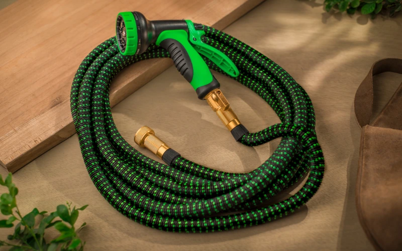 Coiled green expandable garden hose with brass fittings and a spray nozzle.
